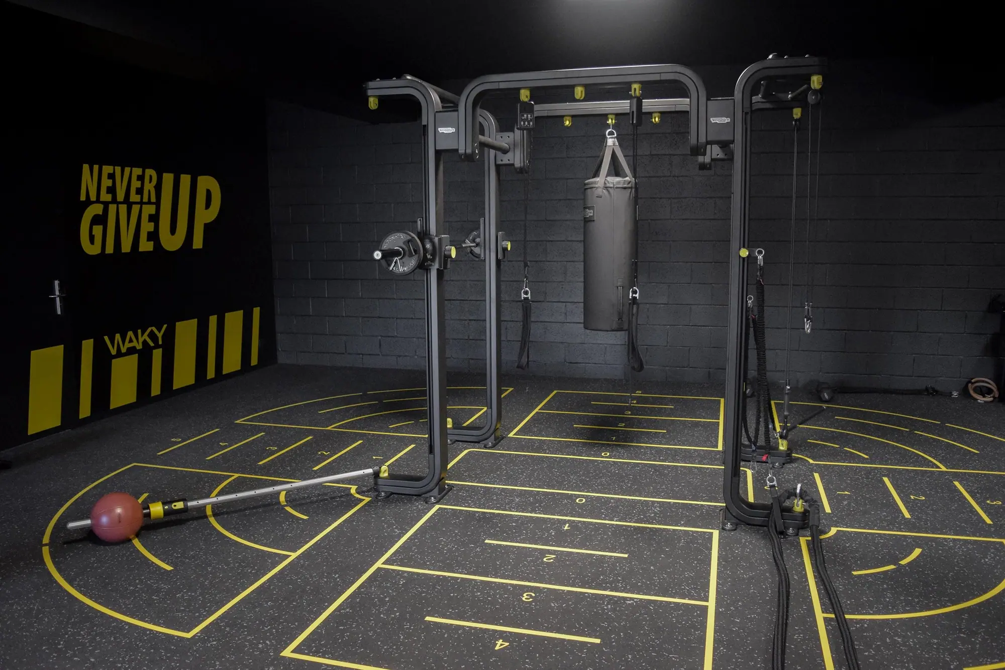 La salle de cross training, sol marqué de jaune, et son mur « Never give up ».